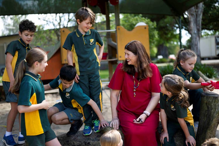 Principal seated and chatting at the sandpit area with students in sport uniform